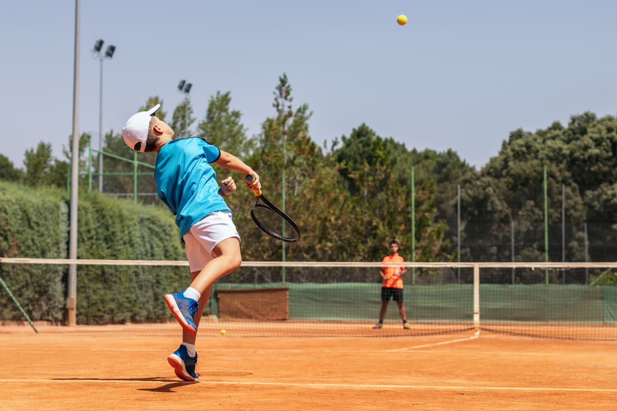 Boy playing tennis with his coach on a dirt court Boy training tennis on a dirt court, he plays against his coach.